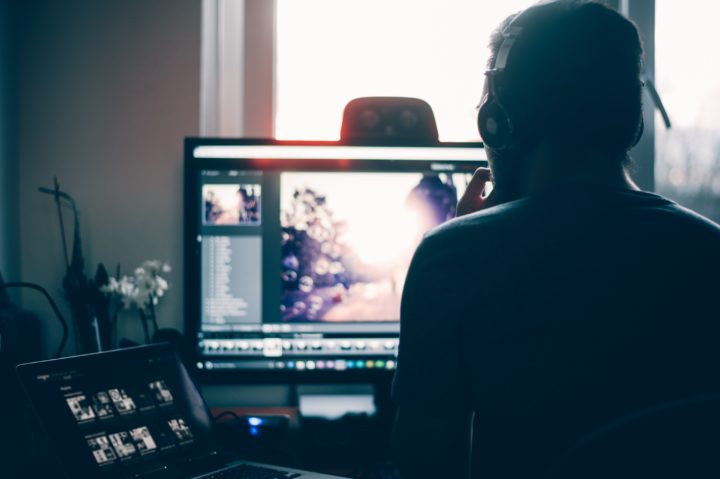 film editor wearing headphones editing a film using two computers