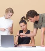 three colleagues discuss something while looking at laptop