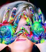 yound child holds paint-covered hands in front of face