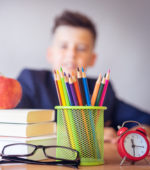 stack of books, an apple, and colored pencils in a cup