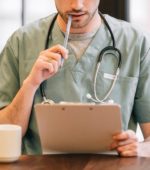 doctor wearing stethoscope examines patient chart