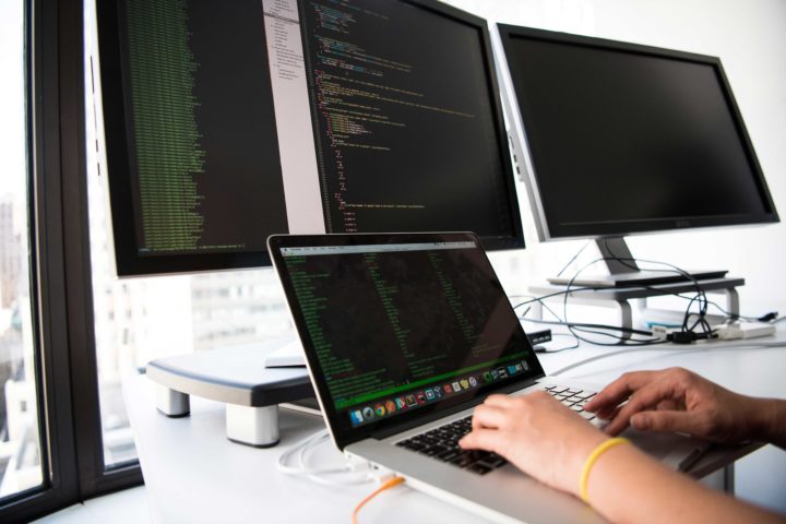Computer Programmer working on a computer using three monitors plus a laptop