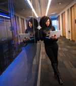 woman in suit stands holding a laptop outside of a blue-lit server room