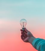 holding lightbulb against pink and blue sky