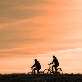 two cyclists riding against a peach sunset