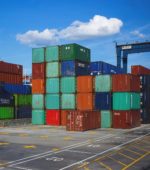 shipping containers of many colors sit on the ground at a dock